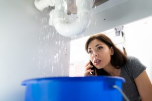 woman-calling-plumber-while-pipe-gushes-water
