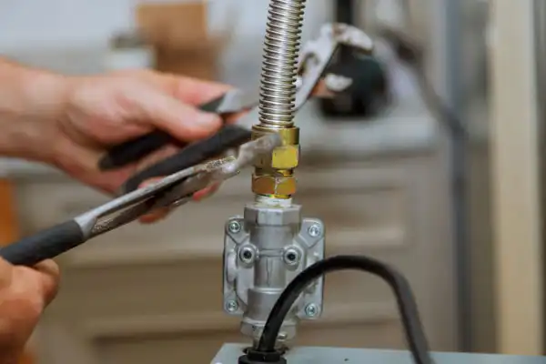 Hands using a wrench to tighten a connection on a metal pipe, possibly part of gas line installation or plumbing, with focus on the tools and fitting.