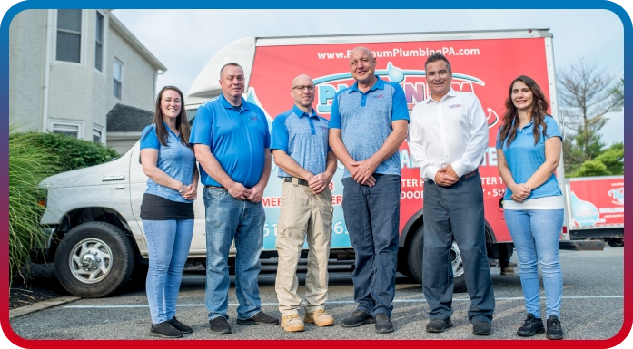 Six people in blue shirts and khaki pants stand in front of a van with "Platinum Plumbing" emblazoned on it, parked outside a building.
