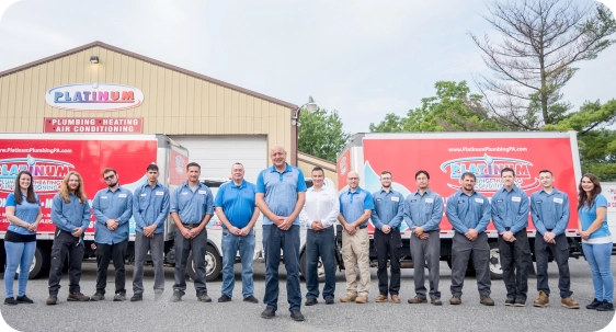 A team of thirteen dressed in matching work uniforms stands proudly before red and white service trucks outside a building, showcasing the excellence of Platinum Plumbing.