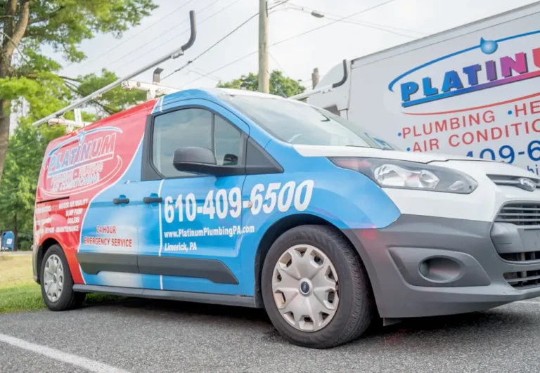 A blue and red Platinum Plumbing van is parked on a road, proudly displaying contact details and service information along its side.